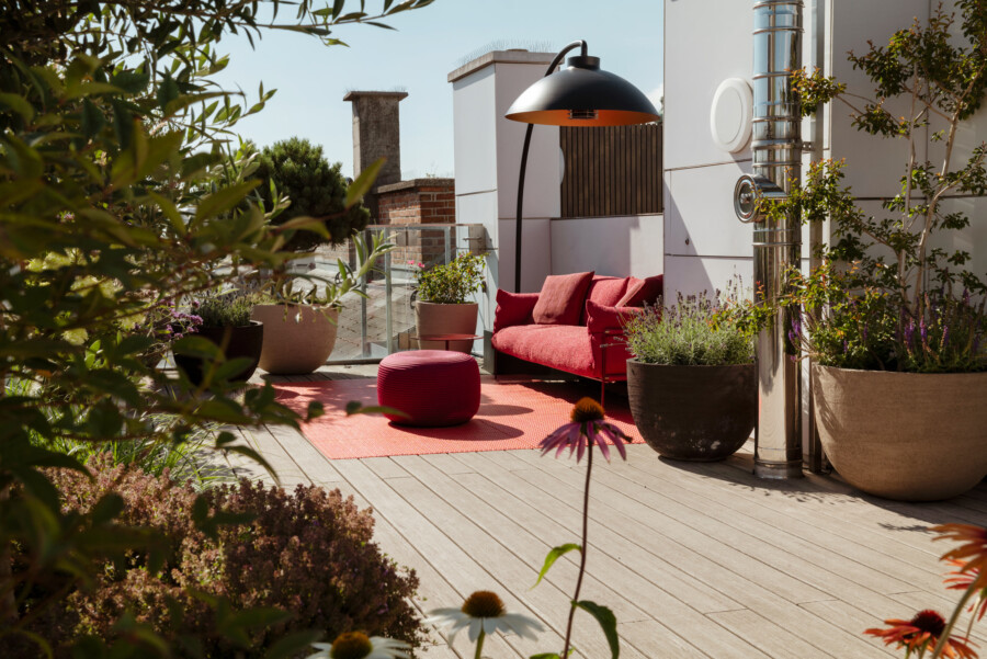 Dachterrasse mit roter Sitzgruppe (Couch, Hocker); Topfpflanzen Olea europaea, Lavandula angustifolia, Lavandula dentata; moderne Edelstahlrohre.