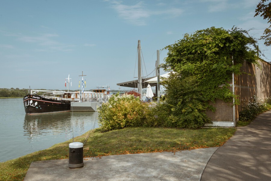 Schiff liegt am Kai des Flusses, Promenade mit Hedera helix (Efeu) an der Mauer, ruhige Szenerie.