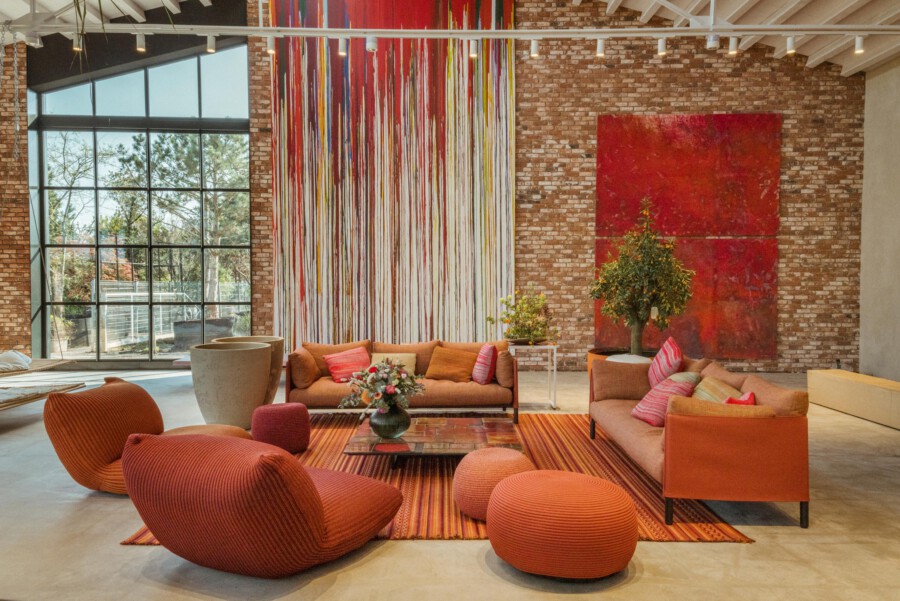 Gemütliche Loft-Lounge: orangefarbenes Sofa-Set, rote Kissen, orange Teppich; Ficus benjamina; rote Wandkunst an Backsteinwand; Glasfront.