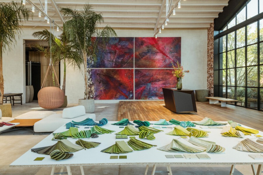 Loftatelier mit Areca-Palme (Dypsis lutescens), großem abstrakten Gemälde in Rot und Blau, Tisch mit Farb- und Stoffmustersammlungen.