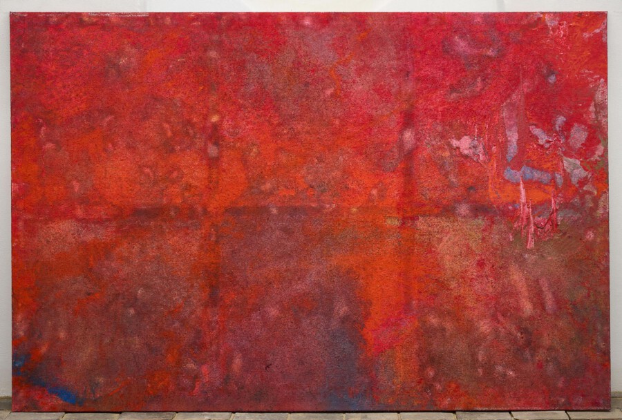 Großes rotes abstraktes Gemälde mit orange- und violetten Nuancen, vor heller Wand auf Pflastersteinen aufgestellt.