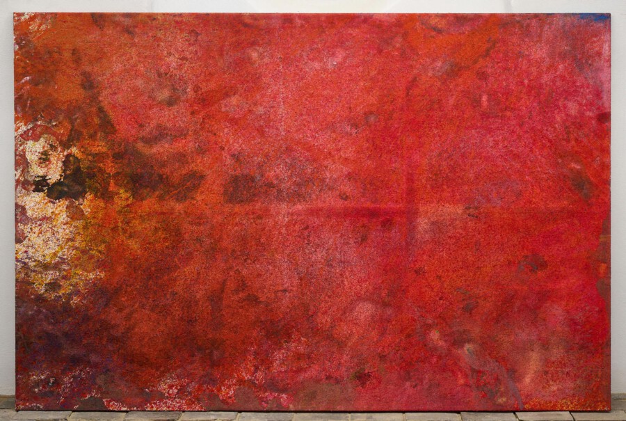 Großes abstraktes Gemälde in Rot- und Brauntönen, an weißer Wand über Pflasterboden gelehnt.