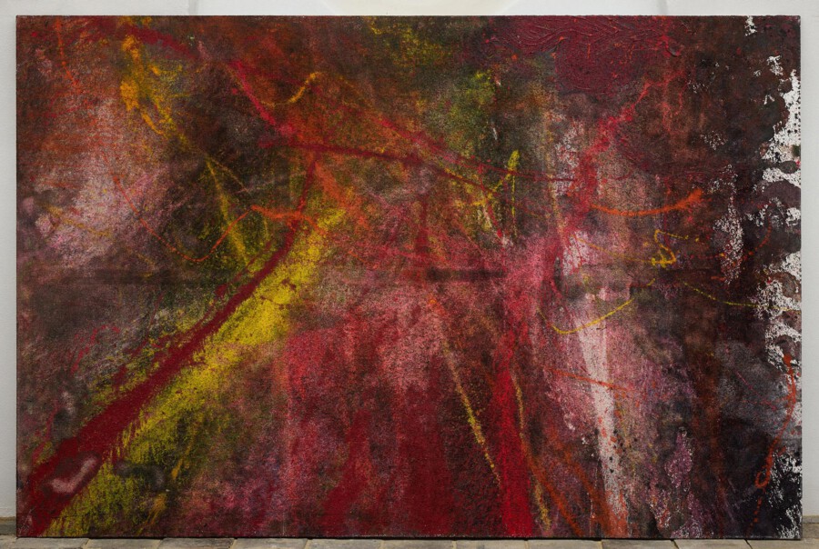 Großes abstraktes Gemälde mit roten, gelben und dunklen Farbschichten; stark texturiert, vor grauer Wand auf dem Boden stehend.