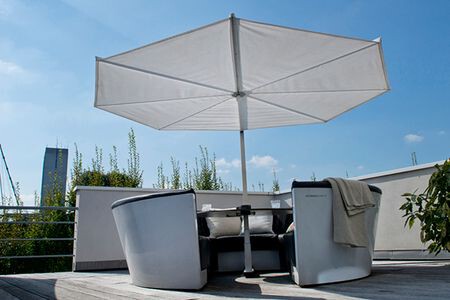 Rooftop patio seating under a large white umbrella; curved cushioned chairs and potted plants along the railing.