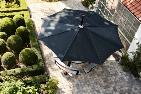 Overhead view of a tiled courtyard with a dark umbrella over a round table and chairs, amid spherical boxwood topiary (Buxus sempervirens).