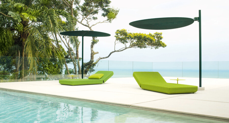 Two lime-green wicker lounge chairs by a pool, tropical palms (Dypsis lutescens) and Colocasia esculenta, glass barrier, distant sea view.