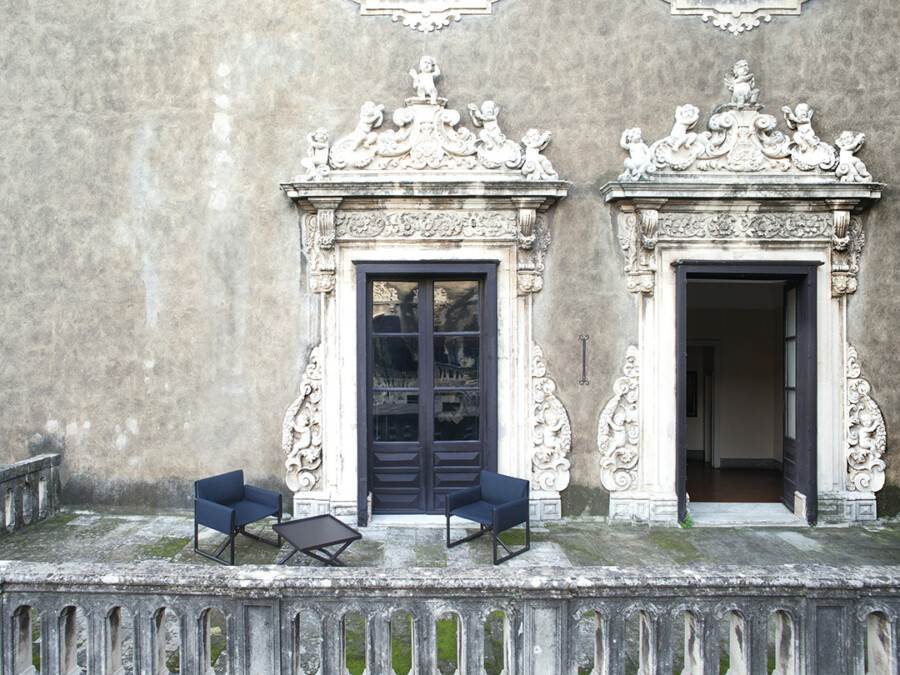 Zwei geschnitzte Barocktüren in Steinfassade; auf dem Balkon stehen zwei dunkelblaue Sessel und ein Beistelltisch.