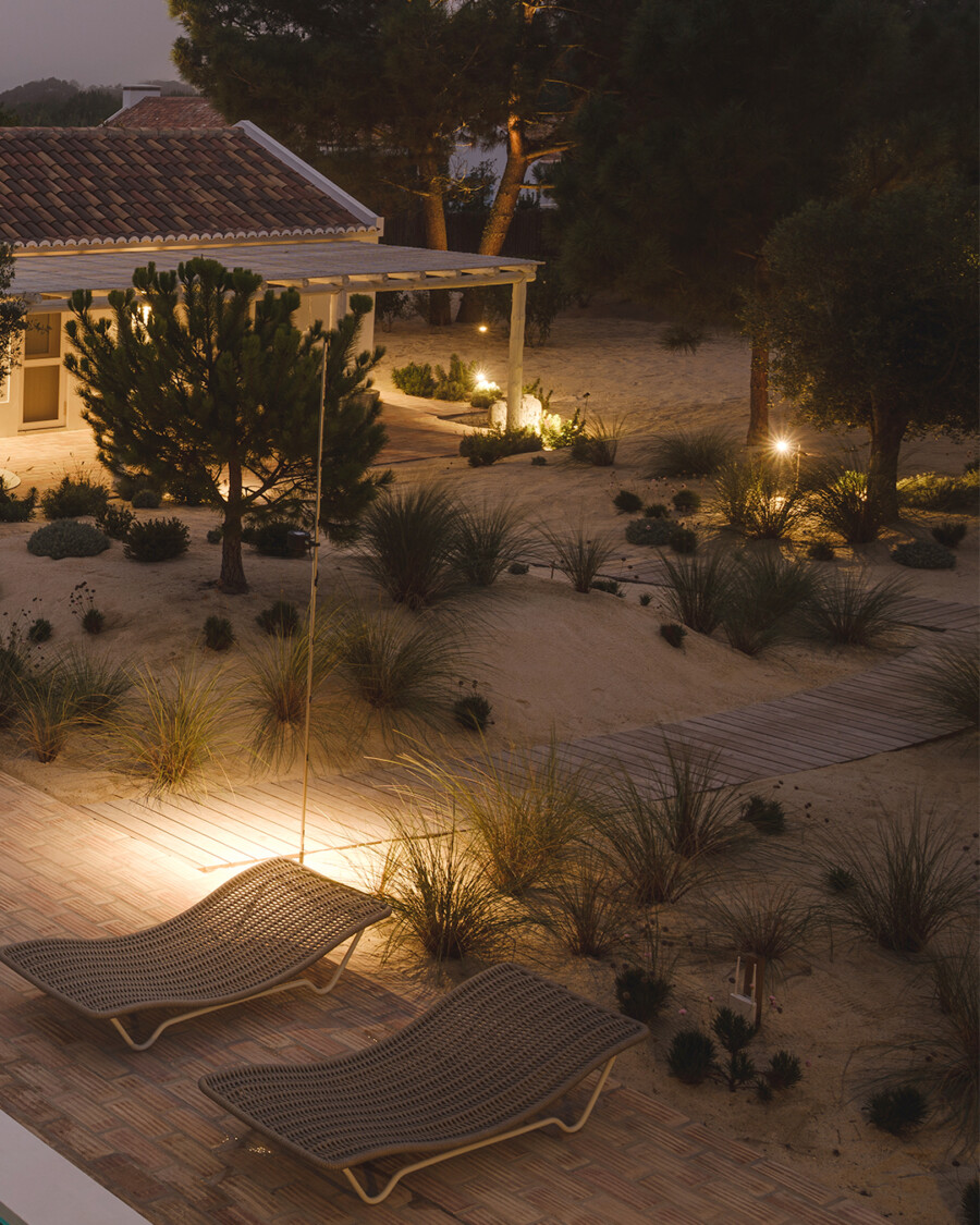 Abendliche Gartenterrasse: zwei Korb-Liegestühle, sandige Beete mit Yucca spp., Pennisetum setaceum und Pinus sp., warmes Licht.