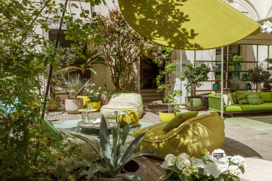 Terrassen-Lounge mit gelbem Sonnensegel; Agave americana im Vordergrund, Cycas revoluta und Rhododendron indicum, grüne Sitzlandschaft.