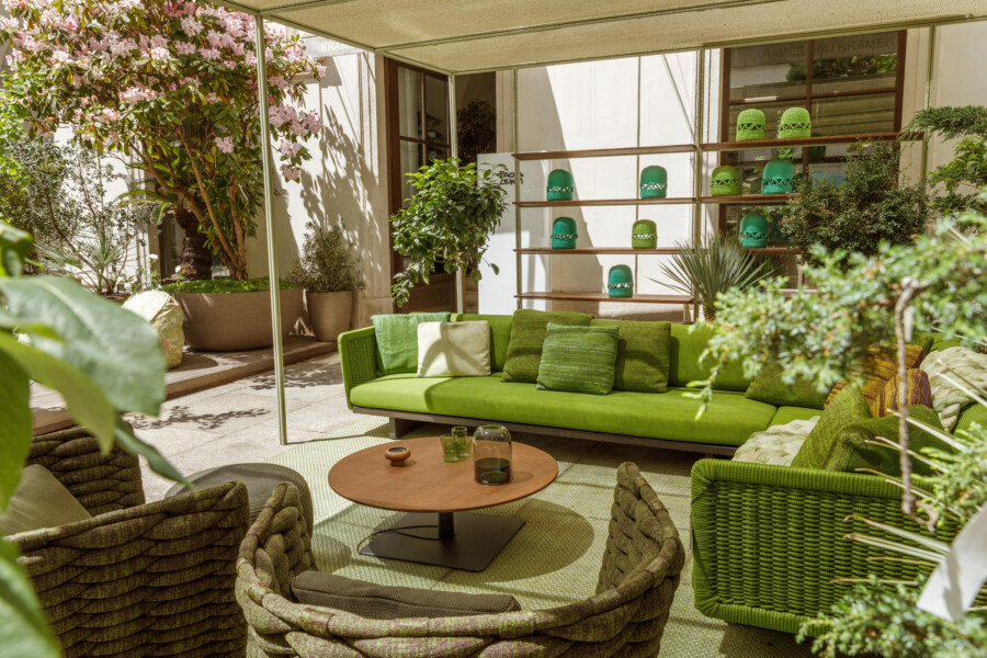Terrassen-Lounge mit grünem Sofabereich und Korbsesseln, runder Holztisch; Bougainvillea spectabilis und weitere Topfpflanzen.