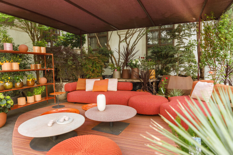 Gemütliche Sitzecke auf überdachter Terrasse; orangefarbene Sofas, runde Tische; Topfpflanzen wie Dracaena marginata, Cordyline sp., Citrus sp.