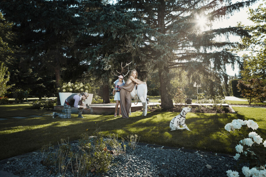 Gartenaufnahme: Fotograf kniet und fotografiert drei Personen in fantasievollen Outfits; eine trägt Hirschgeweih, eine weitere lehnt sich an die erste.