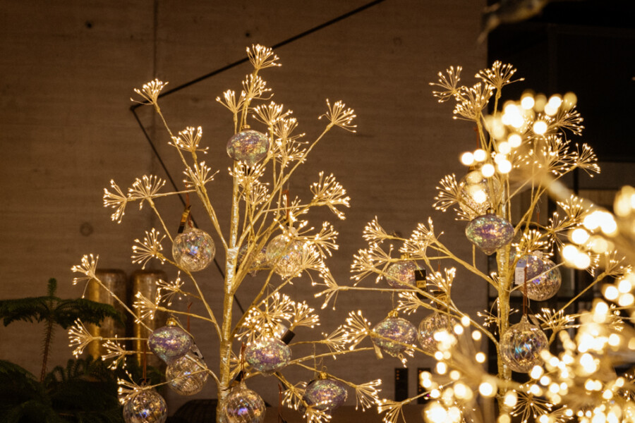 Leuchtende goldene Baumskulpturen mit glitzernden Kugelornamenten, warmes Licht – festliche Innenraumdekoration.