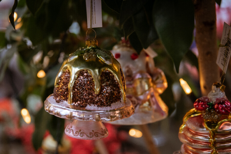 Glas-Glockenornament mit goldener Glasur, rosa Sockel und braun-glitzernden Flächen, an einem Baum mit warmen Lichtern aufgehängt.