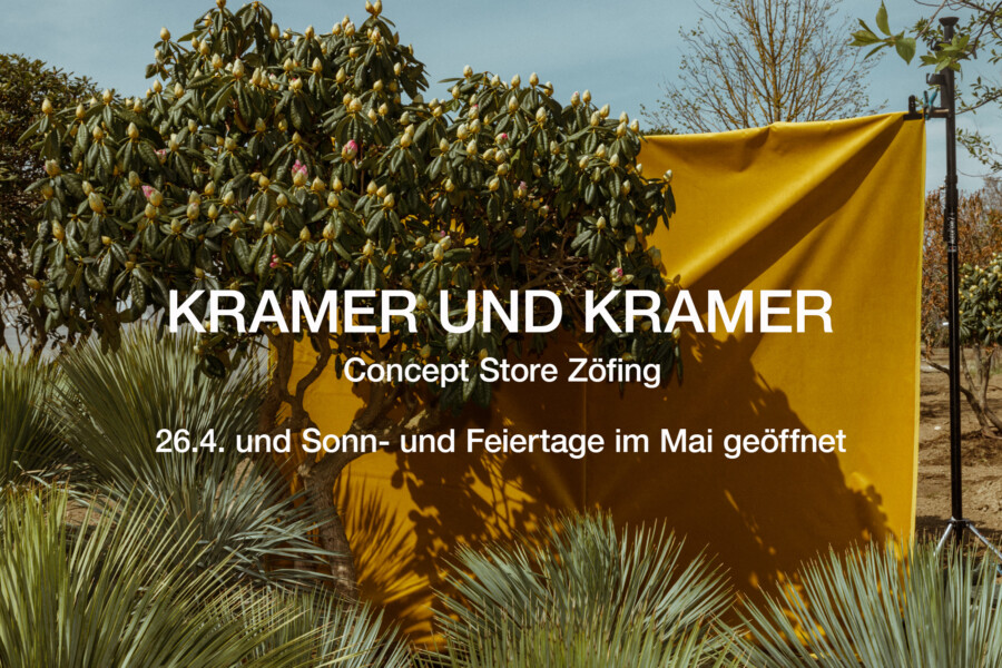 Großes gelbes Werbebanner im Freien vor Yucca sp. und Camellia sp.; Text: KRAMER UND KRAMER gut sichtbar.