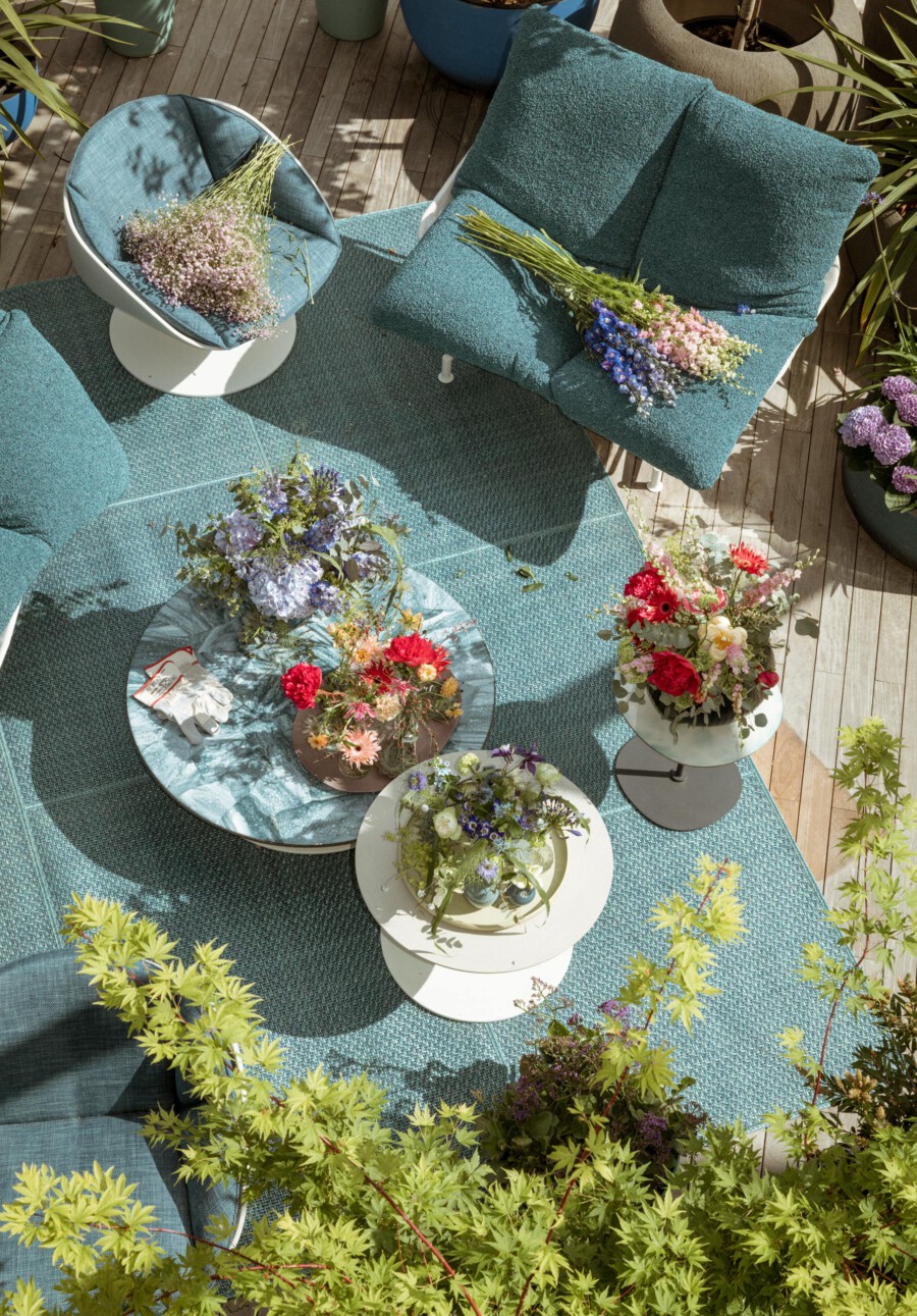 Außenlounge auf Holzdeck mit türkisfarbenen Kissen; Blumenbouquets liegen auf Tischen, darunter Hydrangea macrophylla und Gypsophila paniculata.